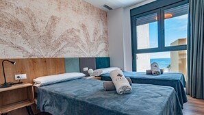 A hotel room with two beds, a large window with a view of the sea, and a wooden headboard. - A016 - ARENAL SUITES - AVANOA (Calpe)