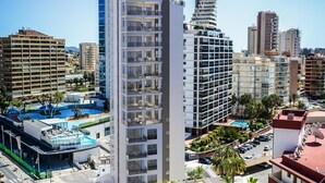 A high-rise hotel with multiple balconies, a swimming pool, and a parking area. - A016 - ARENAL SUITES - AVANOA (Calpe)