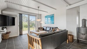 A modern living room with a black leather sofa, a wooden dining table, and a large TV. - Pet friendly home in Vejers Strand (Vejers Strand)