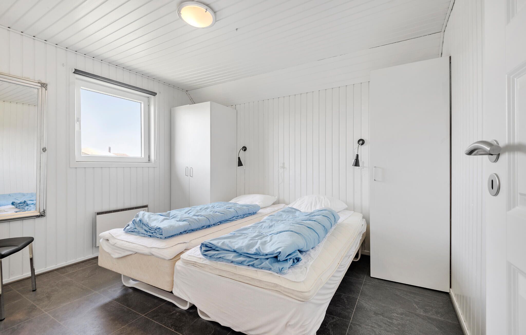 Ett sovrum med två sängar, ett fönster, ett element och en dörr.