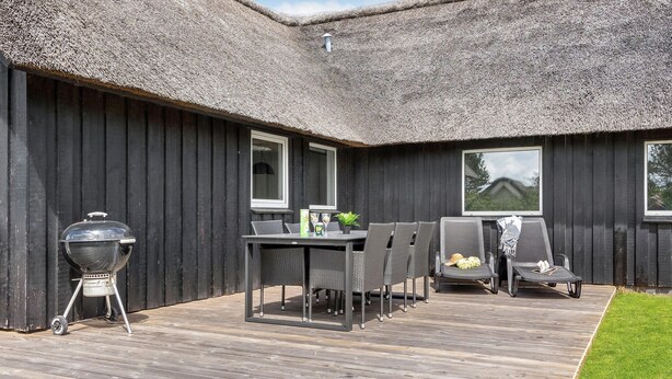 A wooden deck with a table and chairs, a barbecue grill, and a thatched roof structure. - Pet friendly home in Vejers Strand (Vejers Strand)