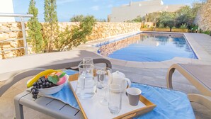 Escena junto a la piscina con una bandeja de alimentos para el desayuno, cielo despejado y un muro de piedra.