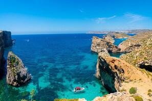 A coastal landscape with clear blue waters, rocky cliffs, and a boat in the sea. - Ta'Siku Gozitan villa + Pool & hot tub (Xaghra)