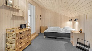 Une chambre à coucher avec un lit, un bureau, un ordinateur, une commode en osier et une porte.