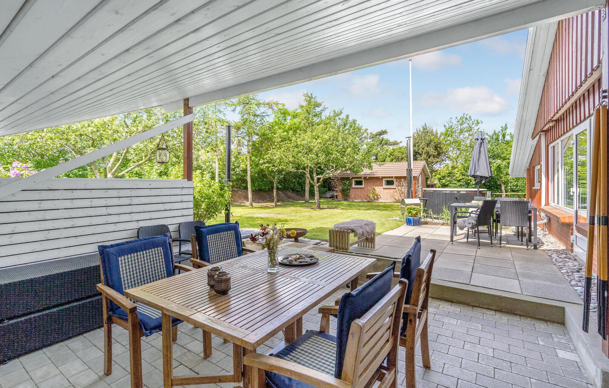 Un espace extérieur aménagé en terrasse, avec une table et des chaises en bois, un coin salon abrité et une vue sur le jardin arrière.
