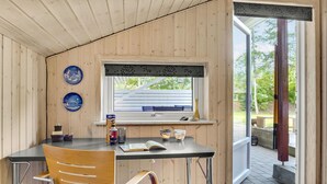 Une pièce chaleureuse au décor intérieur en bois, une petite table avec une chaise, une fenêtre donnant sur l’extérieur et une porte menant à l’extérieur.