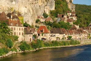 Un village riverain aux bâtiments en pierre, dominé par une falaise imposante et entouré d’une végétation luxuriante.