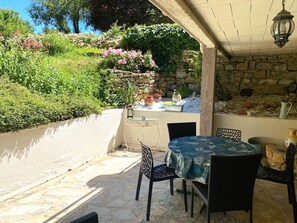 Une terrasse extérieure avec un sol en pierre, une table ronde entourée de chaises et un mur en pierre.