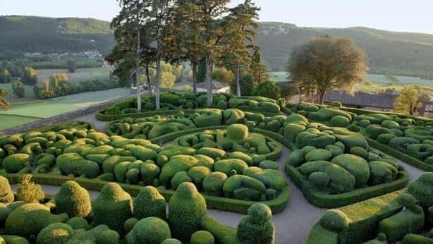 Un jardin aménagé avec le plus grand soin, présentant des motifs géométriques dans les haies et un chemin central.