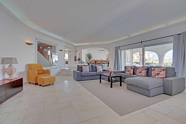 A spacious living room with a sofa set, a yellow armchair, and a dining area in the background.