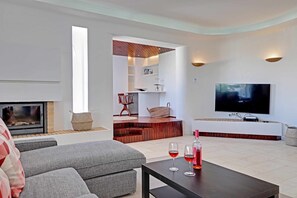 A modern living room with a fireplace, a flat-screen TV, and a dining area with two wine glasses.