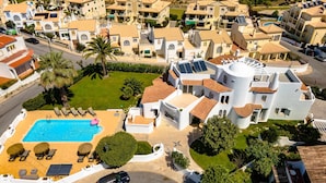 An aerial view of a resort with a swimming pool, sun loungers, and a unique building with solar panels. - Villux - Villa Enar - 6 rooms, ideal for families. (Albufeira)