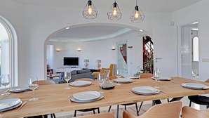 A dining area with a long wooden table set for four, surrounded by chairs. There are hanging pendant lights above the table. - Villux - Villa Enar - 6 rooms, ideal for families. (Albufeira)