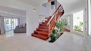 A spacious living area with a wooden staircase, a grey sofa, and a dining area with a glass door leading outside. - Villux - Villa Enar - 6 rooms, ideal for families. (Albufeira)