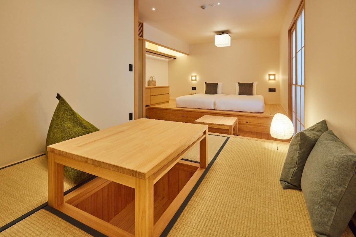 Une pièce de style japonais traditionnel, avec un sol recouvert de tatamis, une petite table en bois, un canapé et un lit avec des oreillers.