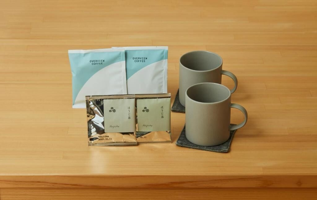 Una mesa de madera con un juego de caf é que incluye dos tazas, dos sobres de café y una caja de cápsulas de café.