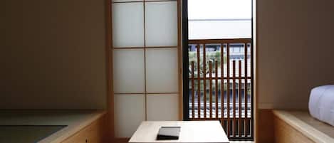 A minimalist room with a tatami mat floor, a low wooden table, and a sliding door leading to an outdoor area.