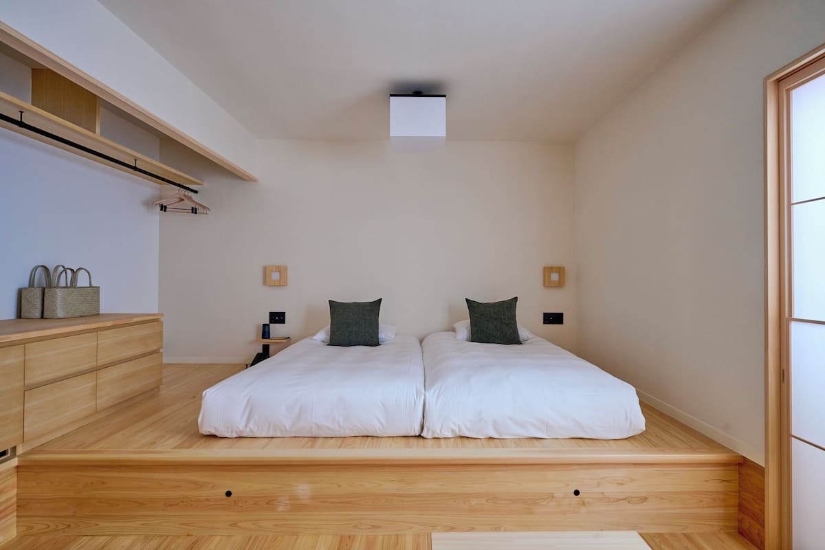Une chambre moderne avec deux lits, un plancher en bois, des étagères intégrées, des tables de chevet et un luminaire au plafond.