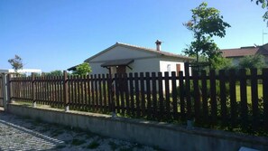 Une maison avec une cour clôturée, un petit jardin et un ciel bleu dégagé.
