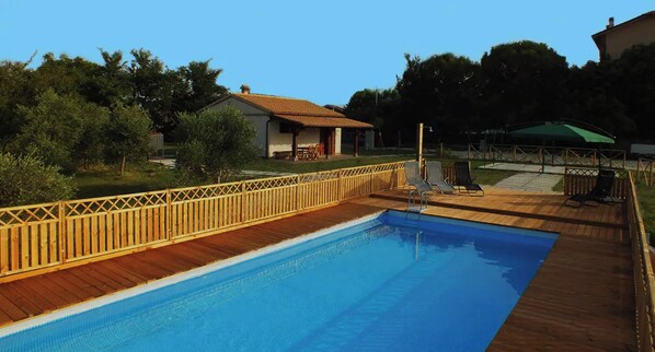Une piscine dotée d’une terrasse en bois et d’une clôture, entourée d’arbres et d’une maison.