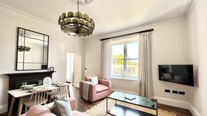 A living room with a fireplace, a pink sofa, a glass coffee table, a TV, and a dining area with a table and chairs.
