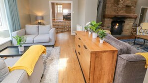 A modern living room with a fireplace, grey sofas, a wooden coffee table, and potted plants. - Burns Cottage (Barnard Castle)