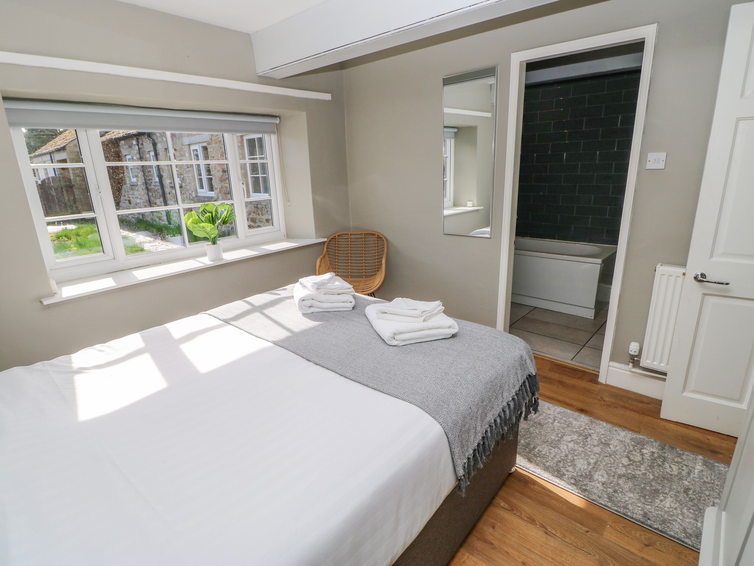 Een slaapkamer met een bed, een raam, een stoel, een spiegel en een deur naar de badkamer.