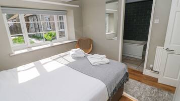 Een slaapkamer met een bed, een raam, een stoel, een spiegel en een deur naar de badkamer.