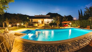 Ein Schwimmbad mit einer Steinterrasse, ein Haus mit einer Veranda und ein roter Schaukelstuhl.