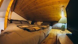 Ein gemütliches Schlafzimmer im Dachgeschoss mit zwei Betten, einer Holzbalkendecke und einem Fernseher auf einem Holztisch.