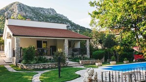 Ein Haus mit einer Steinaußenwand, einem roten Ziegeldach, einem Swimmingpool und einer Bergkulisse im Hintergrund.