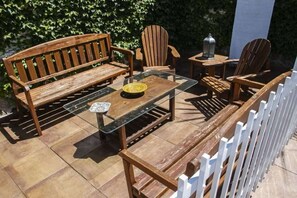 An outdoor patio with a wooden bench, two Adirondack chairs, a glass-top table, and a lantern. - LAS PARRAS (Estación de Brazatortas-Veredas)