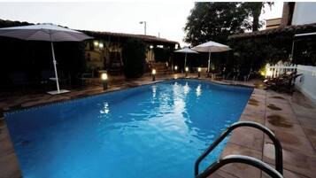 Une piscine dotée d’une terrasse carrelée, entourée de parasols et de chaises.