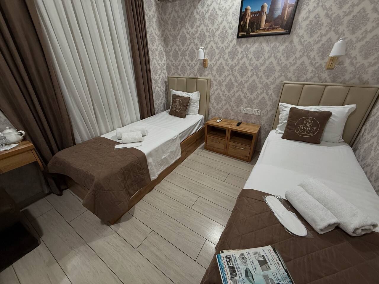 Une chambre d’hôtel avec deux lits, une table de chevet en bois, une petite table et une lampe fixée au mur.