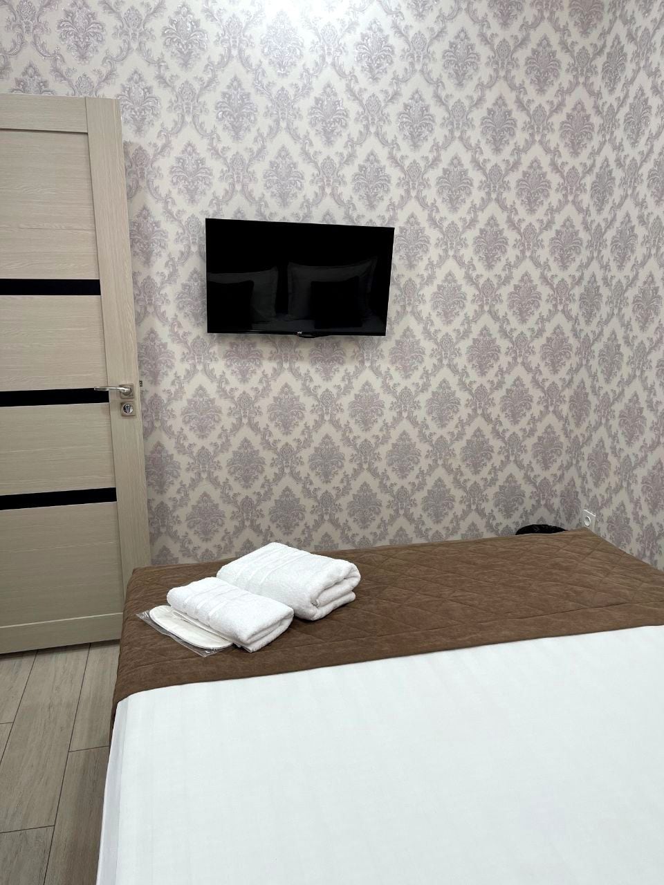 A hotel room with a bed, a television mounted on the wall, and a door.