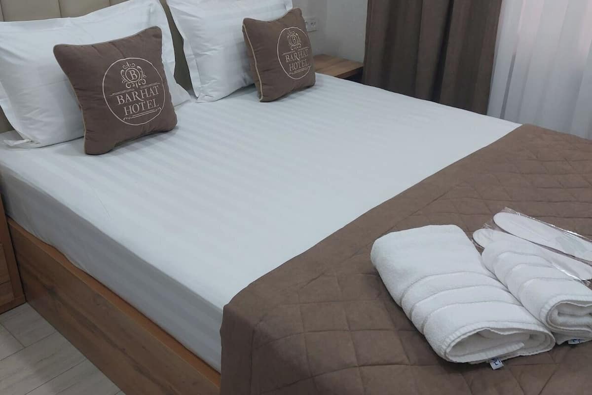 Una cama bien tendida con un colcha marrón, dos almohadas con un logotipo y un juego de toallas a un lado.