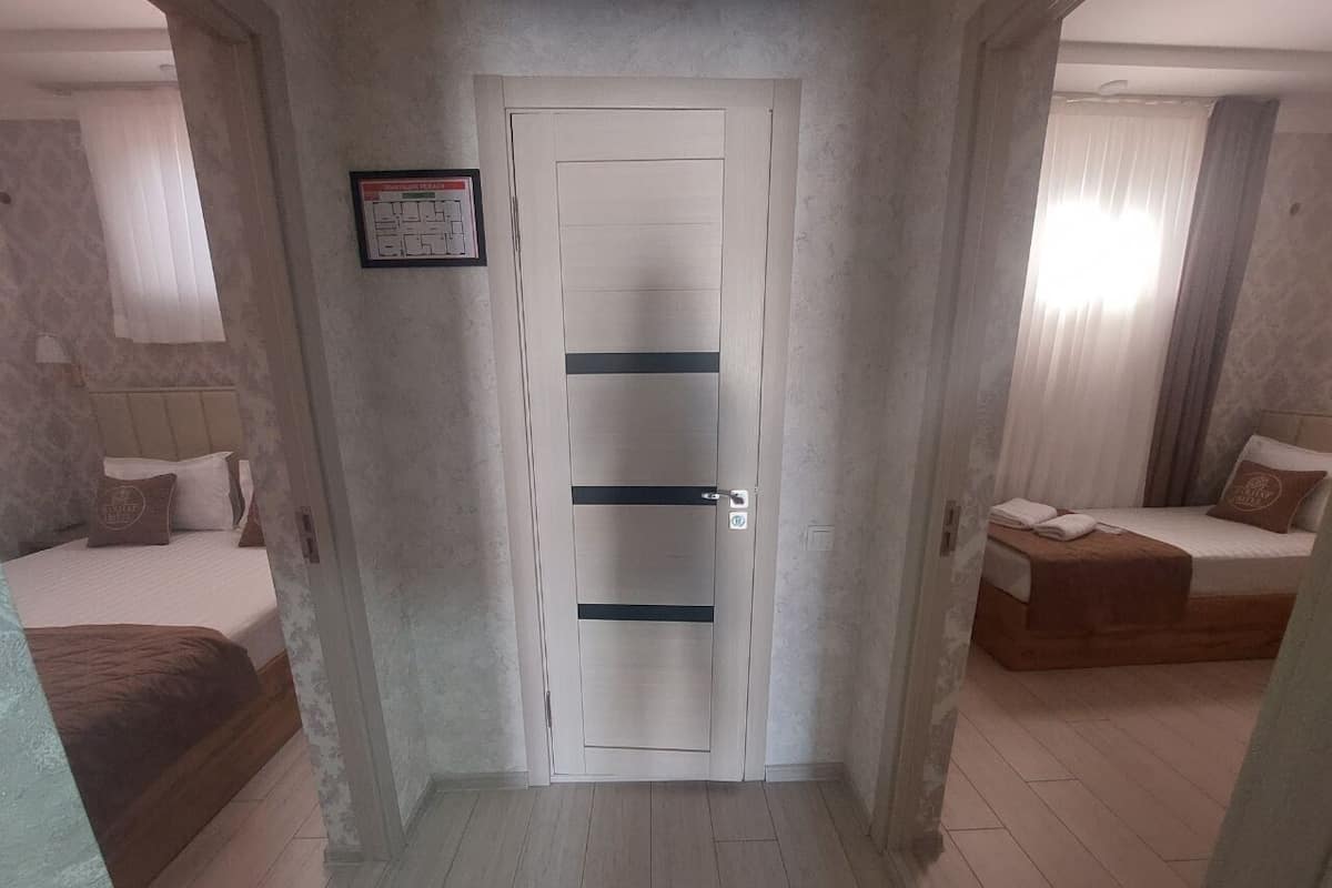 A hallway leading to a bedroom with a bed, a small seating area, and a door with a fire safety sign.