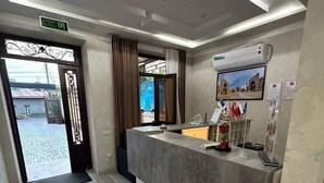 A reception area with a modern design, featuring a reception desk, a digital screen, and a view of the outside through a glass door. - BARHAT HOTEL (Tashkent)