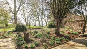 Un jardin avec un mur de pierre, des arbres et un chemin pavé.