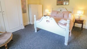 A bedroom with a white bed, two bedside tables with lamps, a chair, a wardrobe, and a painting on the wall. - South Lodge (Appleby-in-Westmorland)