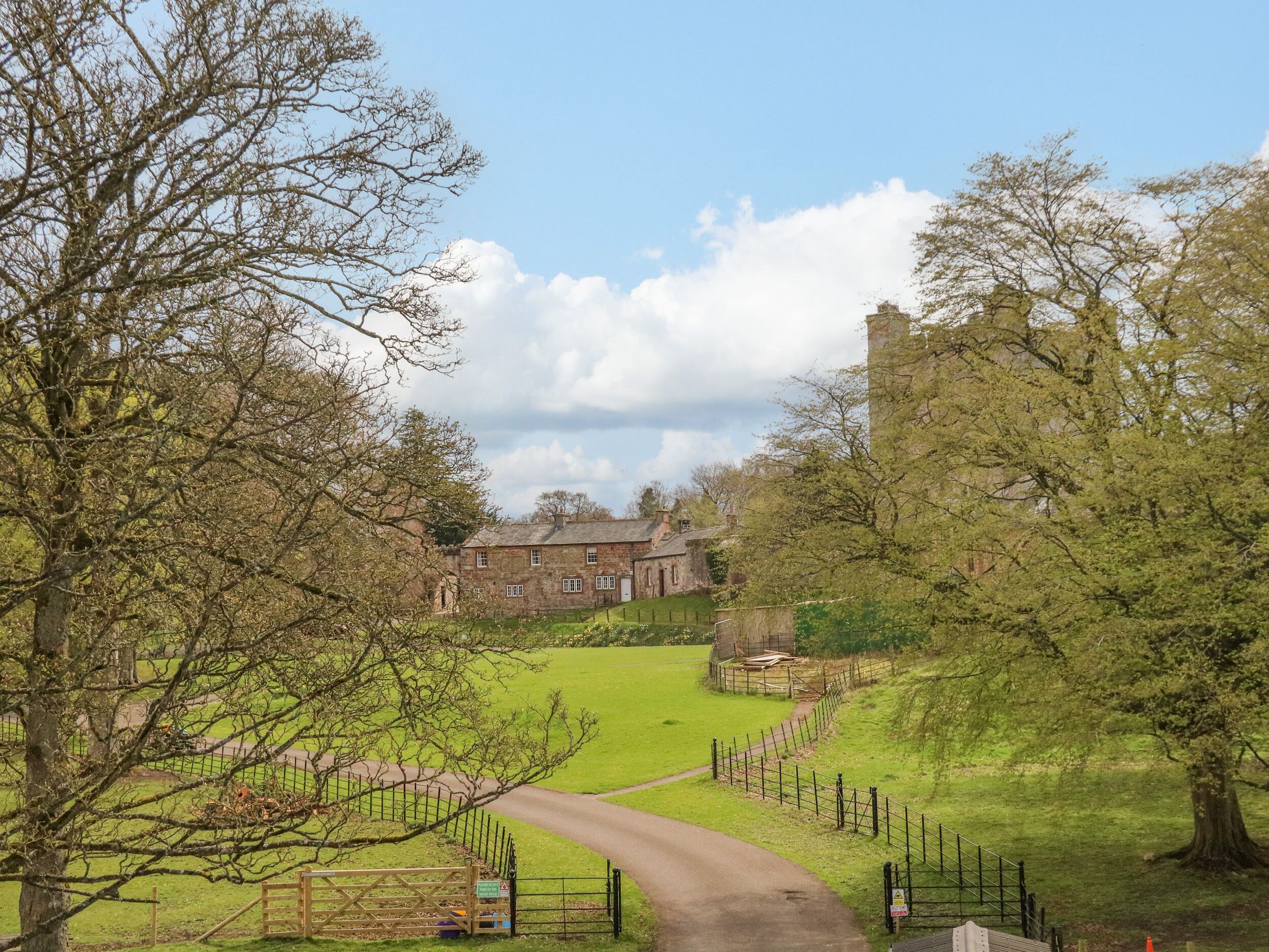 A rural pathway leading to a stone building with a traditional architectural style, surrounded by trees and open fields.