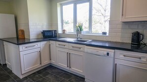 Een keuken met witte kastjes, een zwart aanrecht, een Bosch vaatwasser en een raam met uitzicht op bomen.