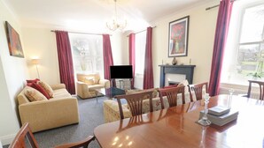 Een woonkamer met een bank, fauteuils, een eettafel met stoelen, een televisie en een open haard.