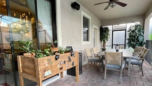 Un espace patio avec une table et des chaises en bois, un banc en bois agrémenté de plantes en pot et un ventilateur de plafond.