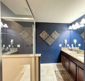 Un baño moderno con pared azul oscuro, dos paneles decorativos, una cabina de ducha de vidrio, un lavabo con encimera de mármol y un espejo grande.