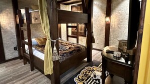 Une chambre avec un lit superposé, un tapis sur le thème de Poudlard, une tête de lit en bois et une petite table avec une lampe.