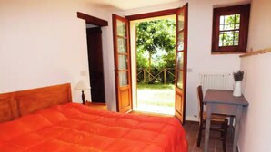 A bedroom with a large bed, an open door leading to a garden, a small table with a chair, and a window with a view of trees. - Farmhouse in the Quiet of the Countryside, Multi-family (Marche)