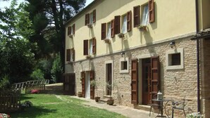 A two-story building with stone walls and wooden shutters, a small outdoor seating area with a table and chairs, and a paved pathway leading to a gate. - Farmhouse in the Quiet of the Countryside, Multi-family (Marche)