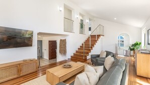 Un vaste espace de vie agrémenté d’un escalier en bois, d’un canapé gris, d’une table basse en bois et d’un grand tableau accroché au mur.
