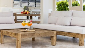 Un salon moderne avec une table basse en bois, deux boissons, un canapé et une cuisine en arrière-plan.